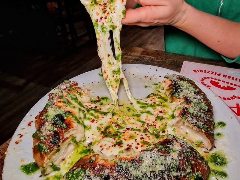 A slice lifted from a pizza, the cheese stretching, with a green pesto drizzle.